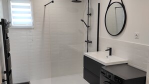 A modern bathroom with a walk-in shower, a built-in washing machine, and a large mirror.