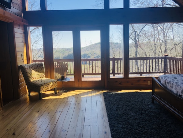 Relax in this cabin with a forest view, featuring a comfortable bed and a spacious deck with a railing.
