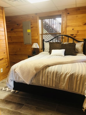 Cozy bedroom with a bed, nightstand, and lamp, set against a wooden ceiling and walls.