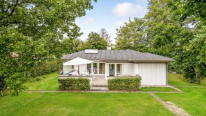 Et etplanshus med en overdækket terrasse, græsplæne og have.