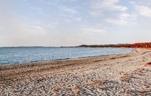 Uma praia de seixos com mar calmo e colinas ao longe.