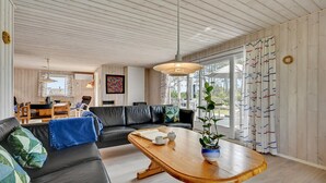 Ett modernt vardagsrum med ett träpanelat tak, en svart lädersoffa, ett träbord och ett stort fönster med gardiner.
