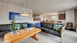 Ett modernt vardagsrum med ett träpanelat tak, en svart lädersoffa, ett träbord och en öppen spis.