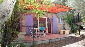 A rustic building with a purple exterior, a red roof, and a small patio area with a table and chairs. - House 55m2, large swimming pool (BUZIGNARGUES)