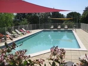 Una piscina rectangular amb vora de rajola, envoltada d'una tanca metàl·lica. Hi ha diverses gandules al costat de la piscina, i una vela ombreig roja és visible en part.