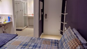 Quarto com cama, mesa de cabeceira, espelho e porta que dá para um banheiro com chuveiro.