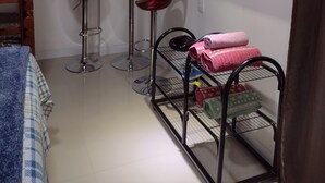 Quarto compacto com cama, televisão, ar condicionado, mesinha e uma cadeira, além de um porta-toalhas de metal.
