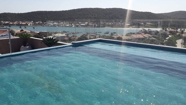 Piscina azul e límpida com vista para uma marina e colinas ao fundo.