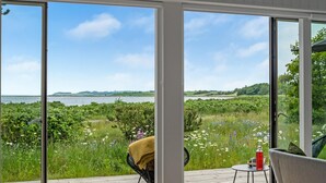 A room with a large glass door leading to a deck overlooking a body of water and a grassy landscape. - Cozy home in Knebel with house sea view (Knebel)