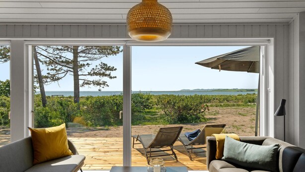 A modern living room with a large sliding glass door leading to a deck overlooking a beach. - Cozy home in Knebel with house sea view (Knebel)