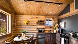 A cozy log cabin interior with a dining area, kitchen, and a large window. - Beautiful Log Cabin in Paradise Valley, Montana (Livingston)