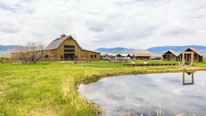 A rustic barn and cabins in a grassy field with mountains in the background. - Beautiful Log Cabin in Paradise Valley, Montana (Livingston)