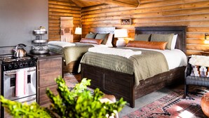 A log cabin-style bedroom with two beds, a kitchen area with a stove, and a small dining table. - Beautiful Log Cabin in Paradise Valley, Montana (Livingston)