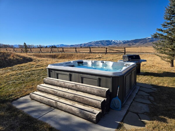 A hot tub with steps leading up to it, a grill, and a view of mountains in the background.