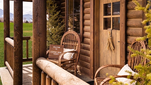 A rustic log cabin with two wicker chairs on the porch, a welcome sign, and a view of the mountains. - Beautiful Log Cabin in Paradise Valley, Montana (Livingston)
