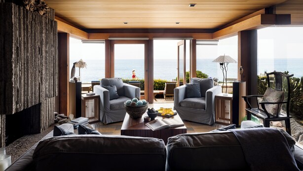 Een moderne woonkamer met een groot raam met uitzicht op zee, ingericht met banken en een salontafel.