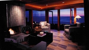 Een moderne woonkamer met een open haard, comfortabele zitplaatsen en uitzicht op de oceaan tijdens de schemering.
