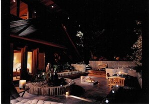 An outdoor patio area with a stone fire pit, wooden seating, and a small waterfall feature. - Architectural Masterpiece on Windansea Beach - Family and Pet Friendly! (La Jolla)