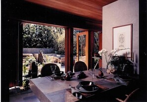 A dining area with a table set for two, a vase with flowers, and a framed picture on the wall. - Architectural Masterpiece on Windansea Beach - Family and Pet Friendly! (La Jolla)