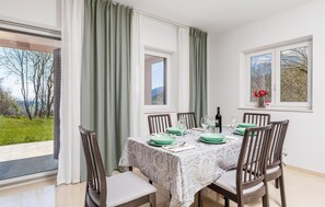 Ein Essbereich mit einem Tisch für vier Personen, umgeben von Stühlen, mit Blick auf Grünflächen und einem Fenster.
