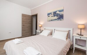Ein ordentlich bezogenes Bett mit weißen Leinentüchern, ein Nachttisch mit Lampe und ein Gemälde einer Berglandschaft an der Wand.
