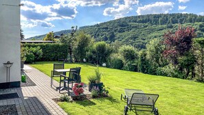 Une terrasse avec une table et des chaises, un petit jardin et une vue sur une colline verdoyante.