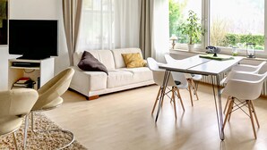 Un salon moderne avec un canapé, une table à manger et des chaises, un téléviseur et une vue sur la verdure par les fenêtres.