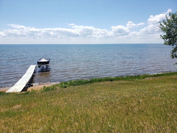 Un muelle que se adentra en un lago tranquilo, con una orilla cubierta de hierba y cielo despejado.