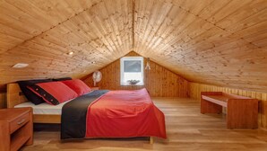 Ein gemütliches Schlafzimmer im Dachgeschoss mit schrägen Wänden, einem Bett mit roter und schwarzer Bettwäsche, einem kleinen Tisch und einem Fenster mit Aussicht.