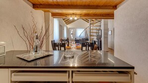 Eine Küche mit Marmorarbeitsplatte, Holzbalken an der Decke und Blick in einen Essbereich mit Treppe.