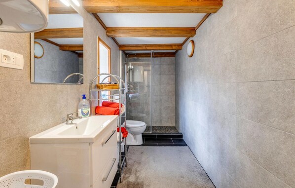 Un baño estrecho con un lavabo blanco, un espejo y una zona de ducha.