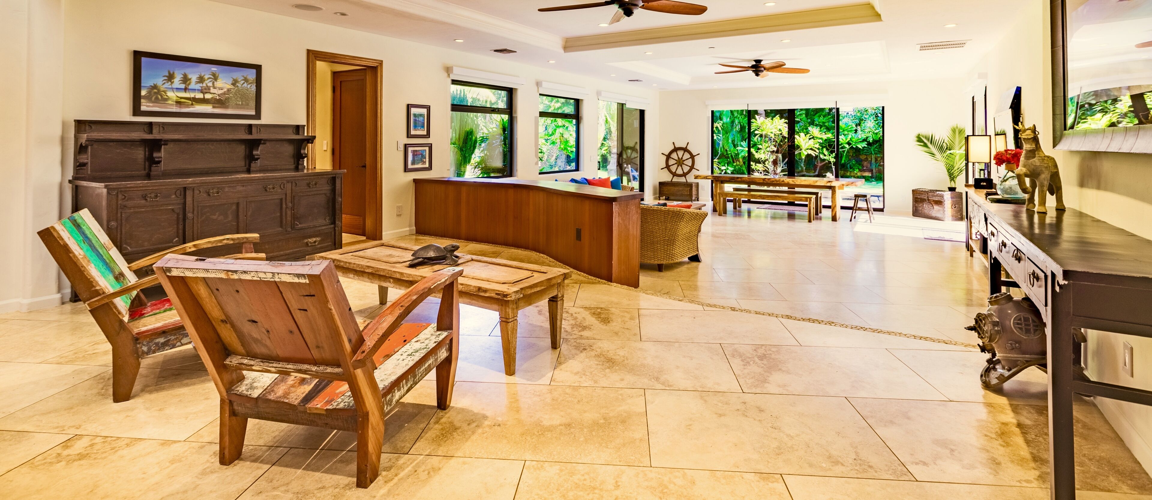 A spacious living area with a wooden coffee table, two wooden chairs, a dark wooden cabinet, and a large window with a view of greenery.