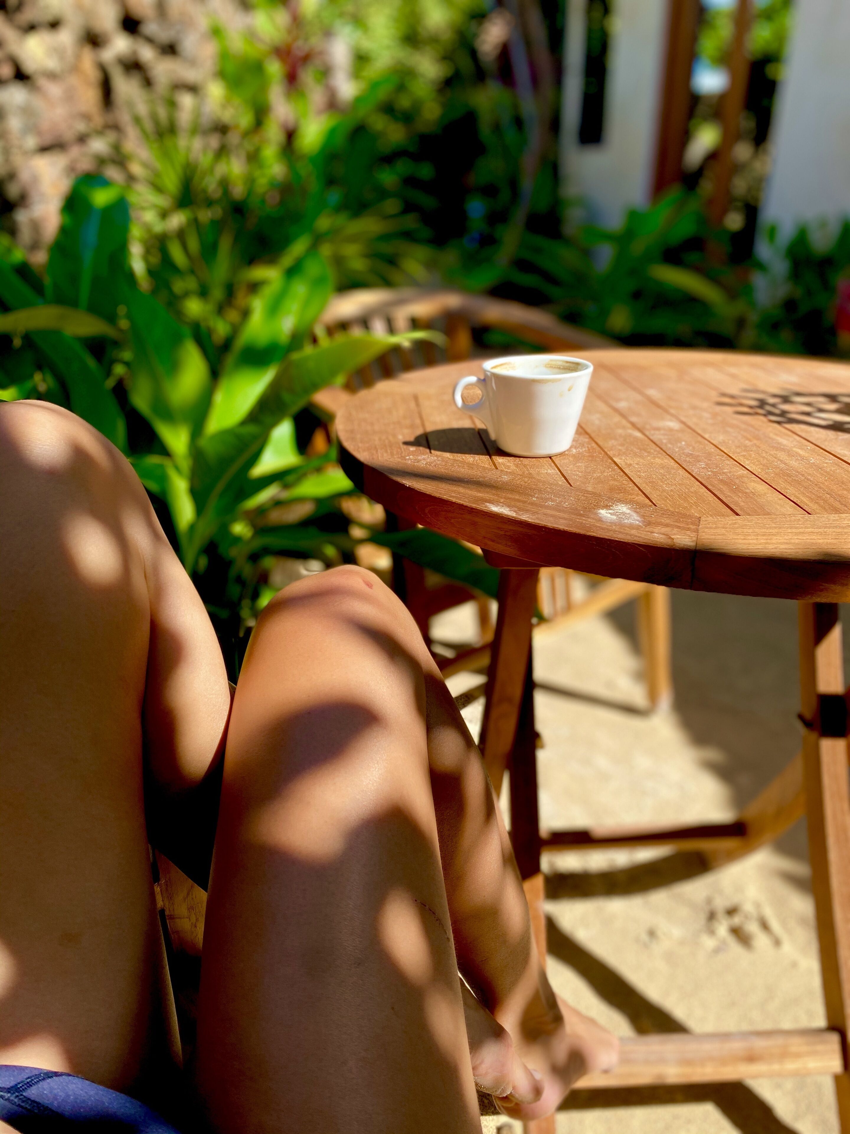 A wooden table with a white cup, surrounded by greenery.