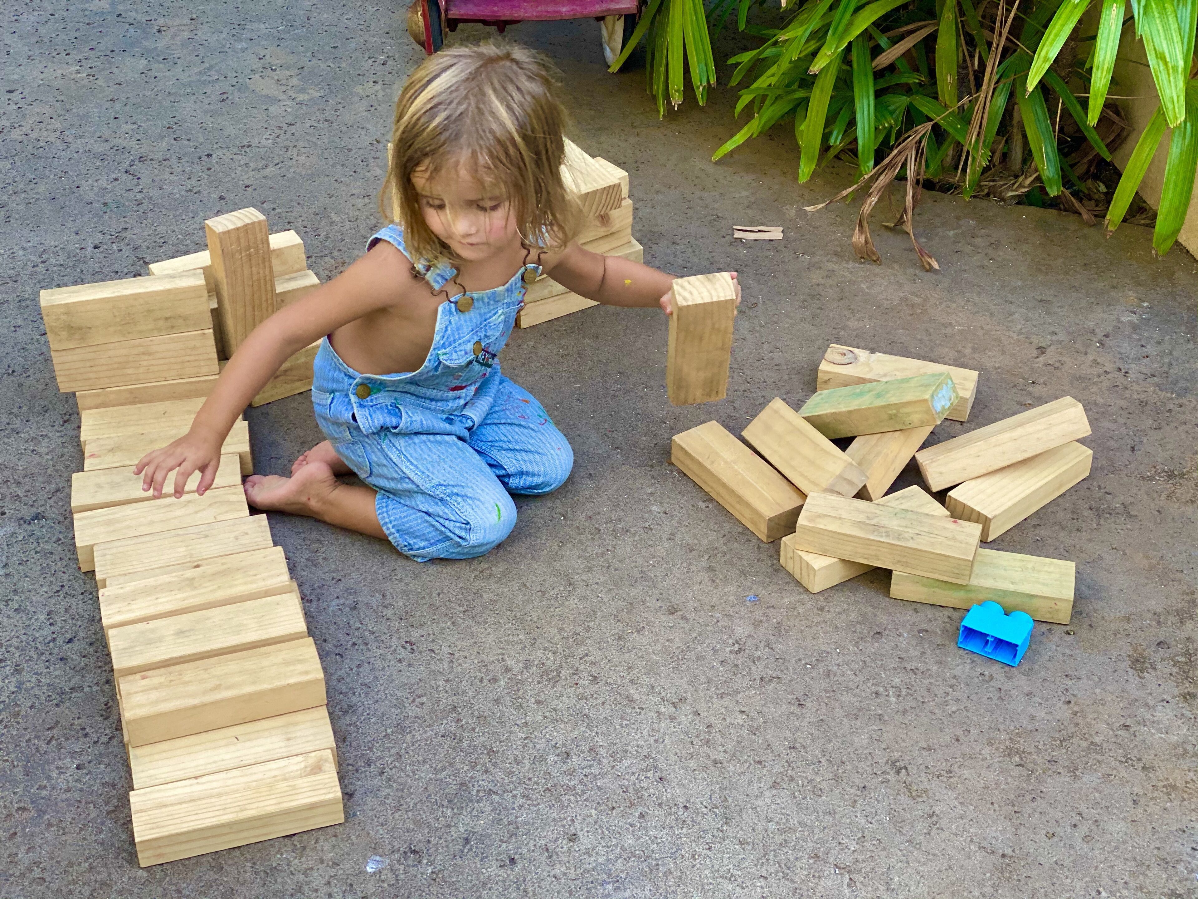A child playing with wooden blocks on a concrete surface.