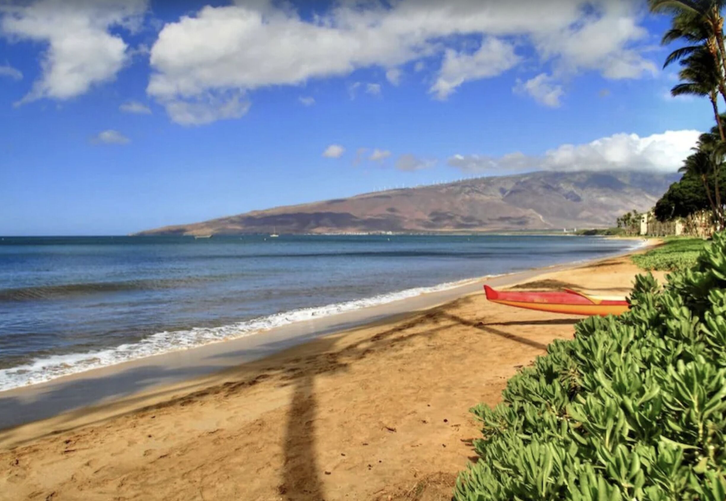A beach with a red kayak, clear sky, and distant mountains.