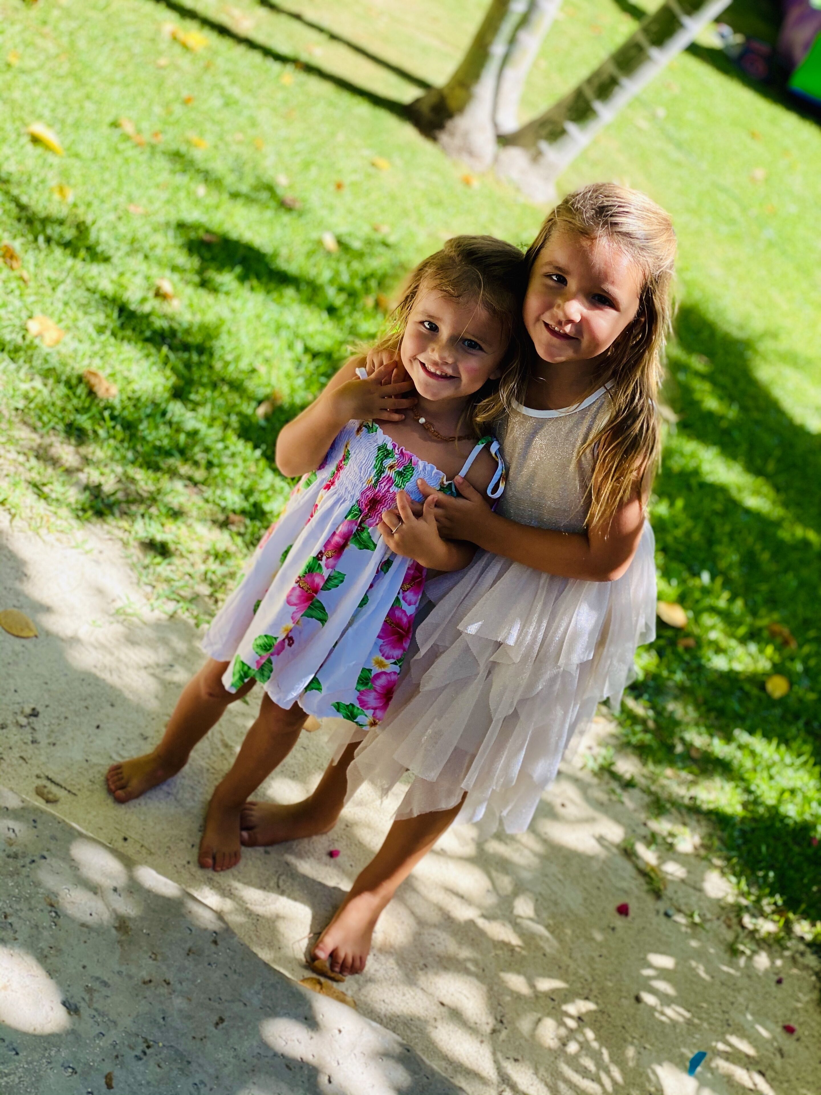 Two children standing on a concrete path with grass and trees in the background.