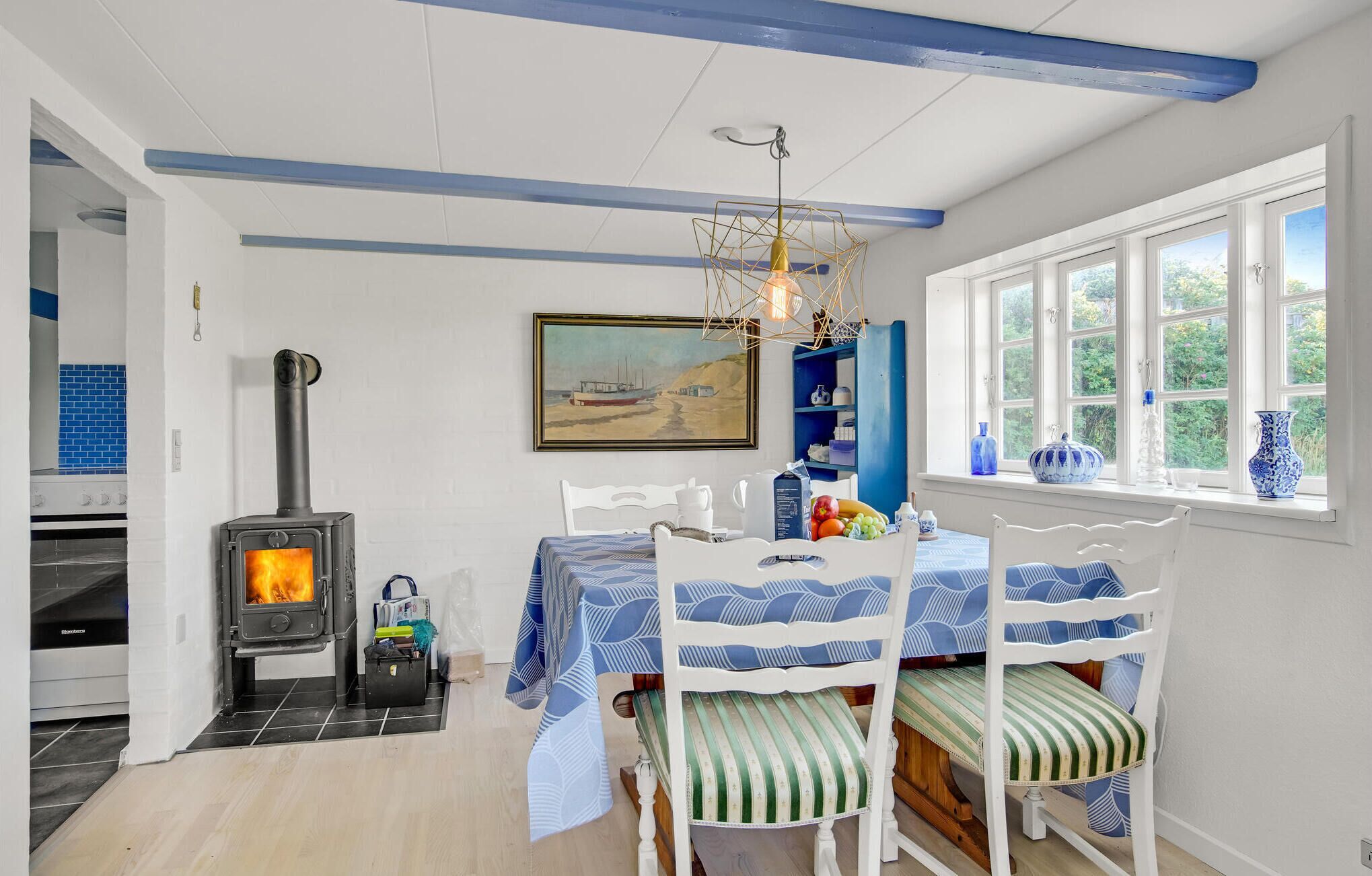 Een gezellige keuken met een houtkachel, een eettafel met stoelen en een raam met uitzicht op groen.