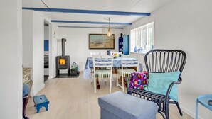 A cozy living room with a wood-burning stove, a dining table with chairs, a colorful armchair, and a window with a view. - 1 bedroom beautiful home in Hjørring (Hjørring)