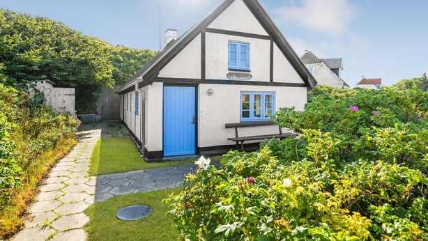 A traditional half-timbered house with a blue door and windows, surrounded by lush greenery and a stone pathway. - 1 bedroom beautiful home in Hjørring (Hjørring)