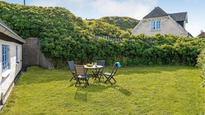 A backyard with a table and chairs, surrounded by lush greenery and a hill in the background. - 1 bedroom beautiful home in Hjørring (Hjørring)