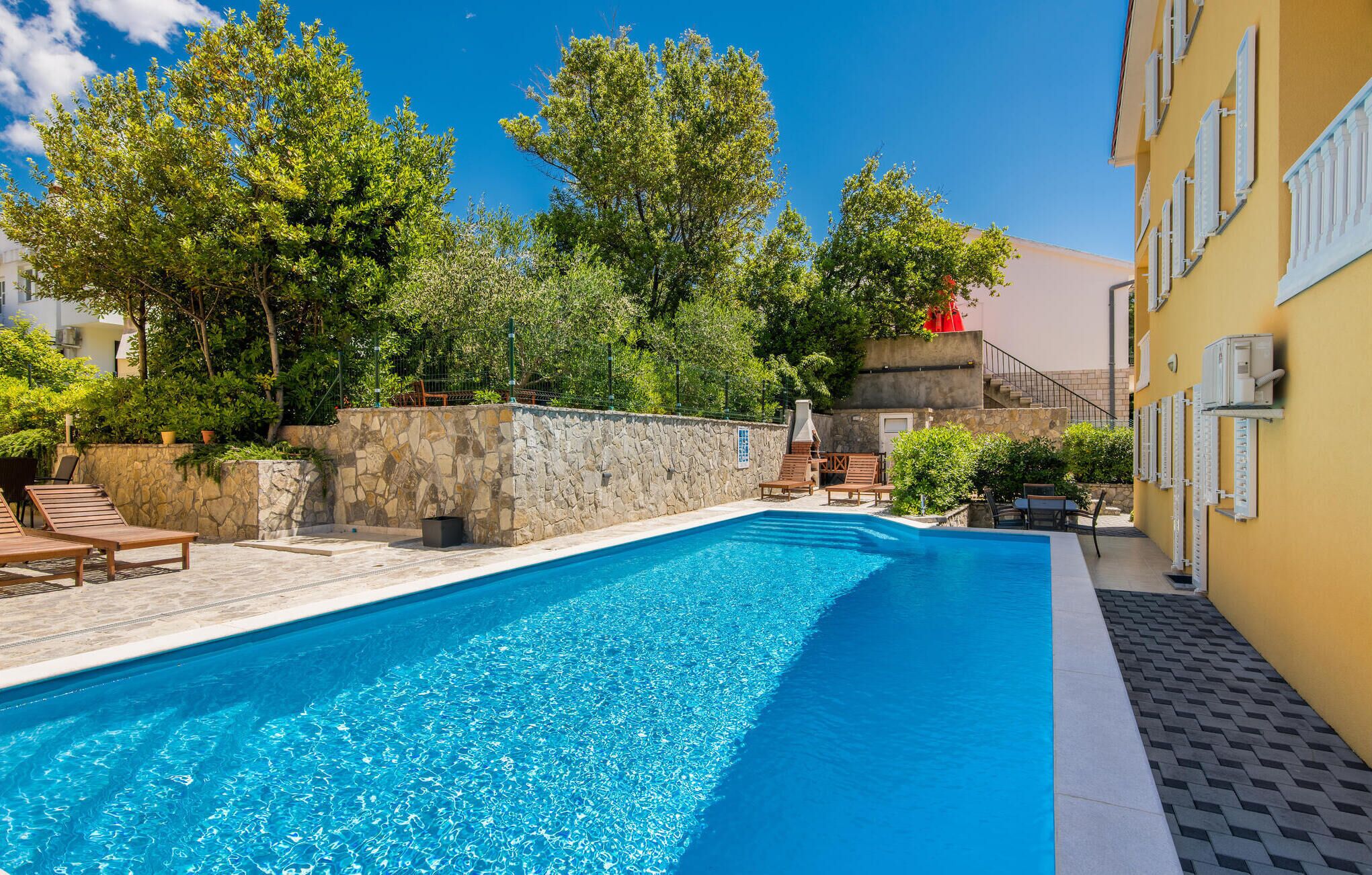 Ein Pool mit Liegestühlen, umgeben von Steinmauern und Grünpflanzen.