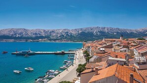 A coastal town with a marina, buildings with red-tiled roofs, and mountains in the background. - Stunning apartment in Baska with WiFi (Baska)