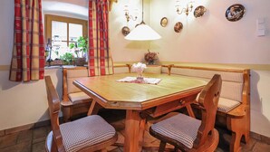 Un comedor con una mesa de madera y seis sillas, una ventana con cortinas a cuadros y platos decorativos colgados en la pared.