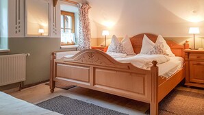 Un dormitorio con una cama de madera, dos mesitas de noche con lámparas, una ventana con cortinas florales y un radiador.