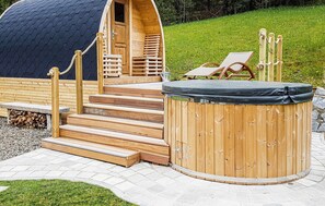 Un bain à remous en bois avec des marches menant à l’intérieur, une terrasse en bois et un fauteuil de relaxation.