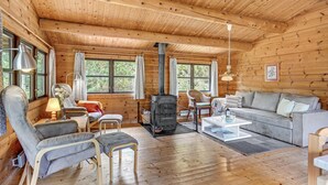 A cozy cabin interior with a sofa, chairs, a table, and a wood-burning stove.
