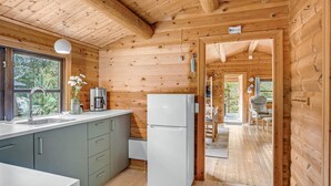 A wooden cabin interior with a kitchen area, including a refrigerator, a coffee maker, and a sink.