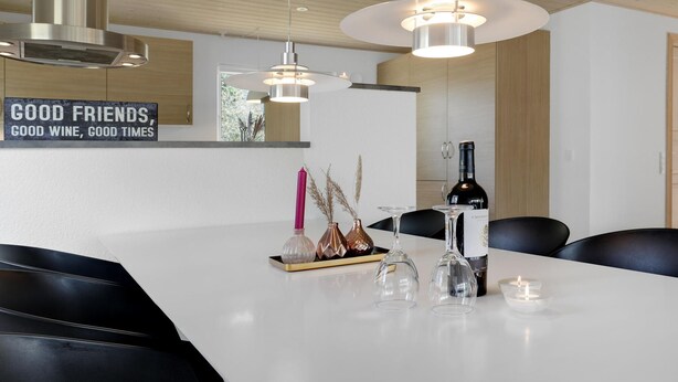A modern dining area with a white table, black chairs, a wine bottle, and decorative items. - 3 bedroom stunning home in Nexø (Nexø)