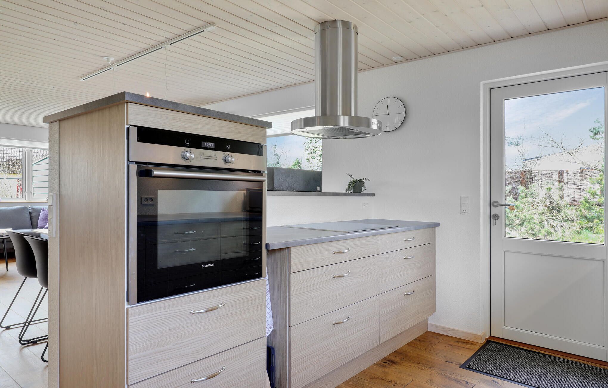 Een moderne keuken met een ingebouwde oven, een roestvrijstalen afzuigkap en een lichtgekleurd aanrecht.