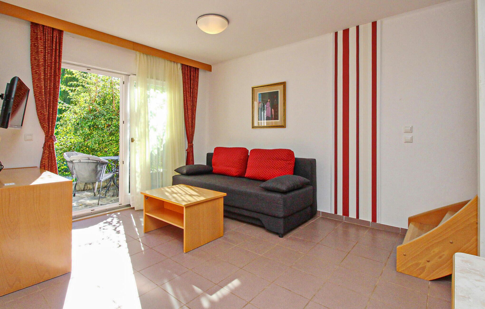 A living room with a sofa, a wooden coffee table, a sliding door leading to a balcony, and a framed picture on the wall.